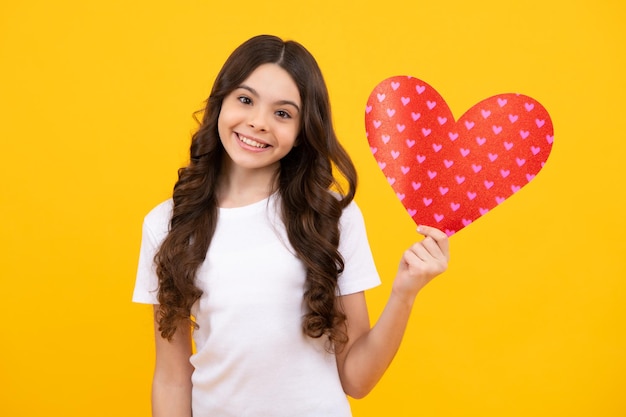 Nastolatka trzyma kształt serca heartshape znak Dziecko trzyma czerwone serce miłość wakacje walentynki symbol odizolowany na żółtym tle Szczęśliwy nastolatek pozytywne i uśmiechnięte emocje nastolatki
