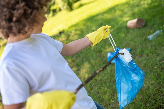 Nastolatka trzymająca kij i zbierająca śmieci na trawie