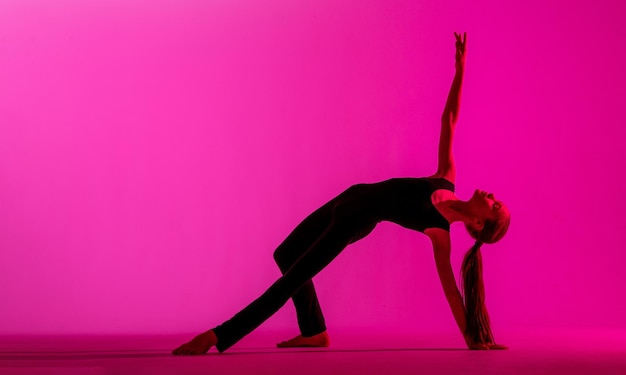 Nastolatka w ciasnym czarnym kostiumie tańczy współczesną współczesną tancerkę odizolowaną na tle w neonowym świetle