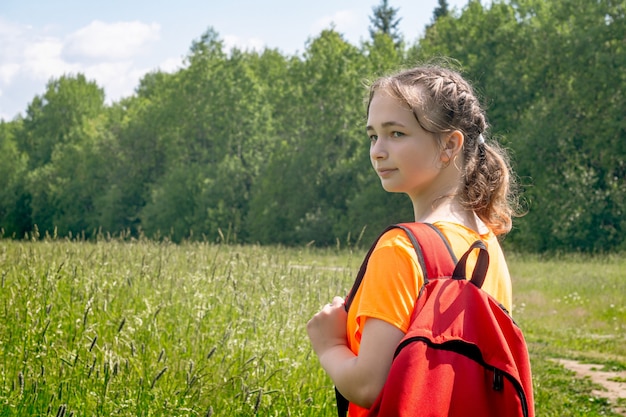 Nastolatka w jasnopomarańczowej koszulce z plecakiem spaceruje w naturze