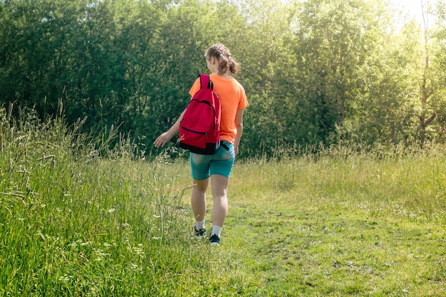 Nastolatka w jasnopomarańczowej koszulce z plecakiem spaceruje w naturze