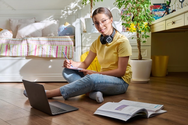 Nastolatka w okularach studiuje w domu za pomocą laptopa