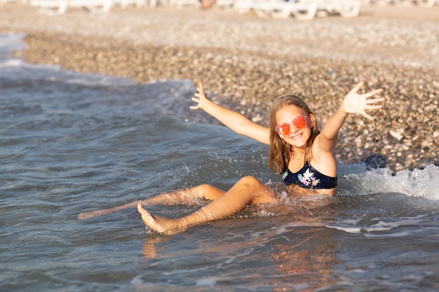 Zdjęcie nastolatka w różowych okularach przeciwsłonecznych bawiąca się na plaży w morzu z odpryskami zabawa na koncepcji letniego hloday