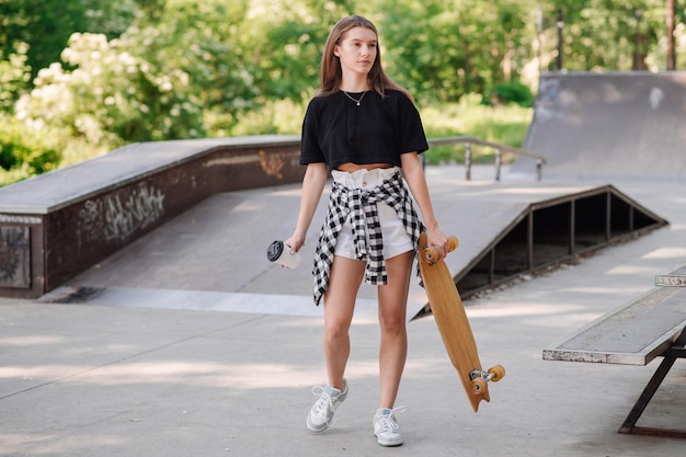 Nastolatka z deskorolką i trzymająca filiżankę kawy spacerująca po skateparku