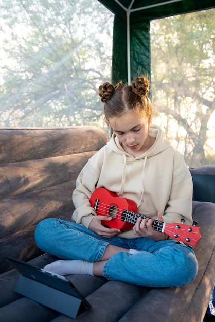 Nastolatka z małym ukulele gitarowym komunikuje się online za pomocą gadżetu.