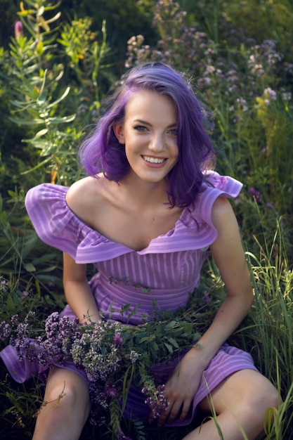 Nastolatka z ufarbowanymi na fioletowo włosami i przekłutym nosem w trawie z bukietem kwiatów i w krótkiej sukience