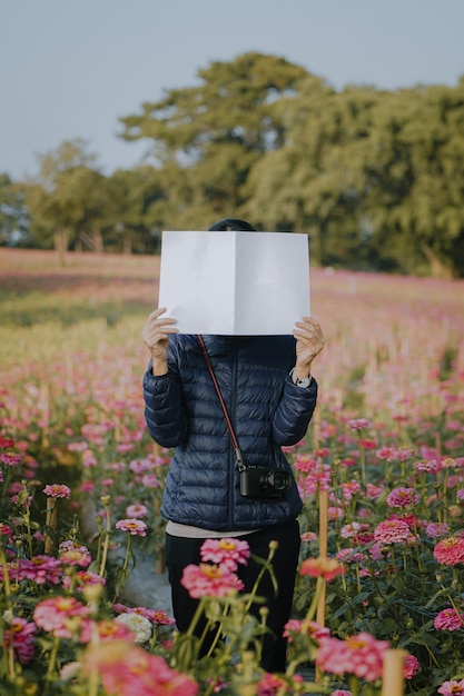 Nastolatka zakrywająca twarz pustą książką lub magazynem z polem kwiatów cyni.