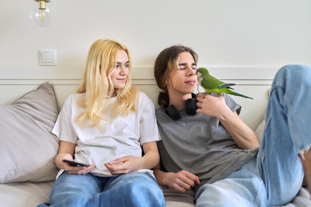 Nastolatki siedzą w domu na kanapie bawiąc się papugą