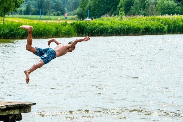 Nastolatki wskakują do wody i pływają w jeziorze w upalny letni dzień Aktywny wypoczynek na otwartym stawie Dzieci wskakują do wody i wykonują różne akrobacje