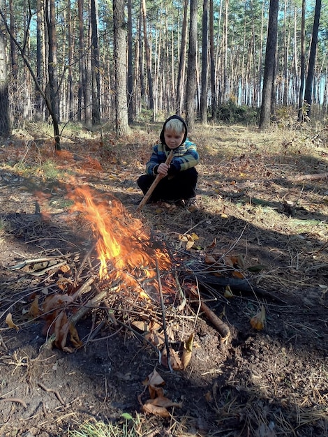 Nastoletni chłopiec rasy kaukaskiej grzeje się przy płonącym ogniu Jest w lesie i ma ufarbowane włosy