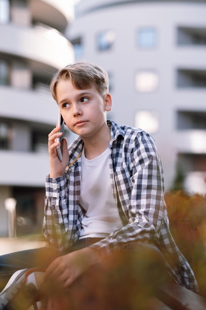 Nastoletni chłopiec rozmawia przez telefon w środowisku miejskim, siedząc na ławce