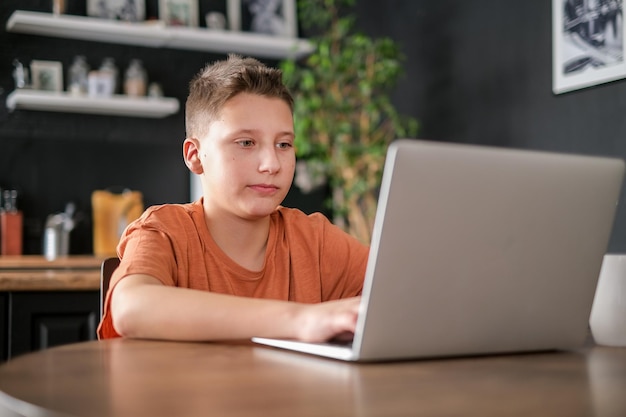 Nastoletni chłopiec studiuje lub gra w grę na tle wnętrza domu laptopa