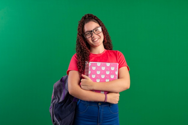 Nastoletni student w okularach, w torbie szkolnej i zeszytach pozuje na zdjęciu studyjnym z zielonym tłem idealnym do kadrowania