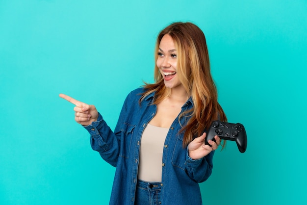 Nastoletnia blondynka bawi się kontrolerem gier wideo nad odizolowaną ścianą, wskazując palcem w bok i prezentując produkt