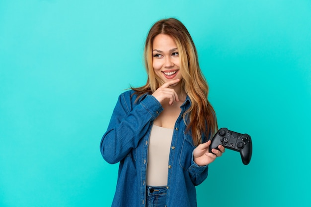 Nastoletnia blondynka bawi się kontrolerem gier wideo nad odosobnioną ścianą, patrząc w bok i uśmiechając się