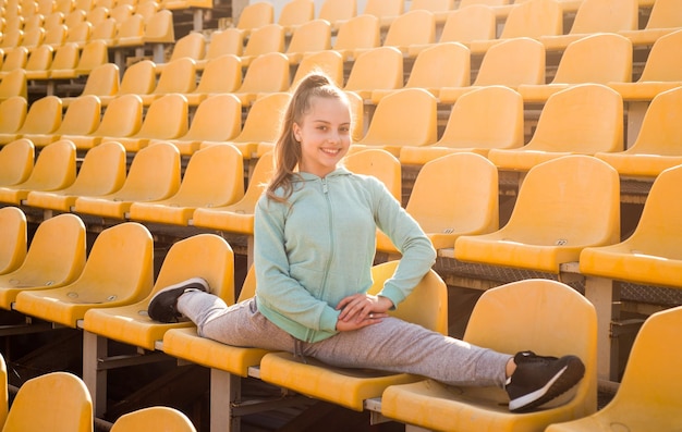 Nastoletnia dziewczyna rozgrzewa się na stadionie dziecko w sportowej odzieży rozciąganie dziecko ćwiczy dzielone na trybunach zdrowe dzieciństwo trening na świeżym powietrzu na świeżym powietrzu pewna gimnastyczka z elastycznym ciałem