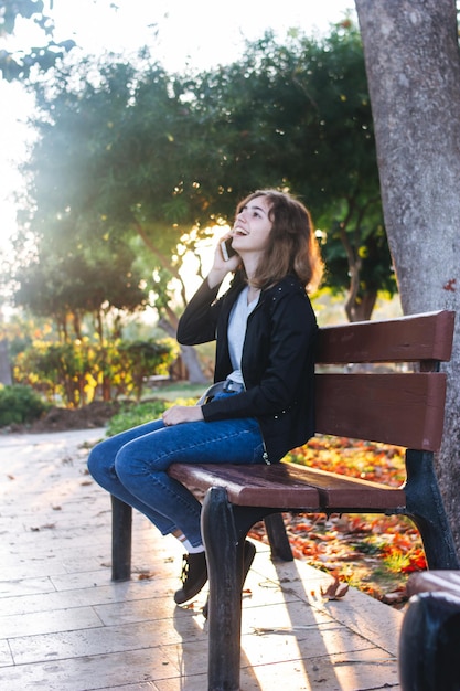 Nastoletnia dziewczyna rozmawia przez telefon na ławce w jesiennym parku