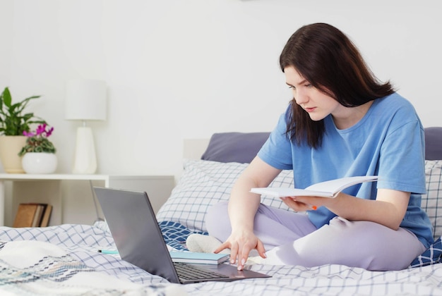 Nastoletnia dziewczyna uczy się w domu na łóżku z laptopem