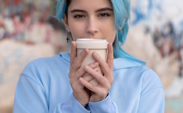 Nastoletnia dziewczyna w jasnoniebieskiej oversize'owej bluzie z kawą na wynos i wyglądająca prosto