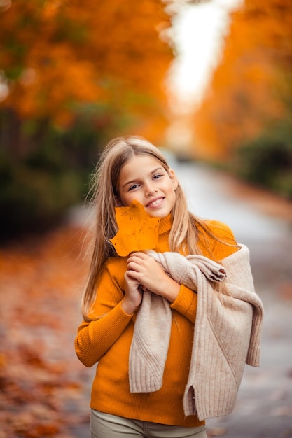 Zdjęcie nastoletnia dziewczyna w żółtym swetrze idzie ulicą poza miastem na tle żółtych drzew zabawny spacer jesienią
