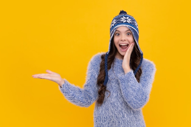 Nastoletnia dziewczyna z kapeluszem zimowym nad odizolowanymi żółtym tłem Zimowe święta Bożego Narodzenia nastrój nowego roku Ciepłe ubrania dla dzieci Podekscytowana nastolatka dziewczyna