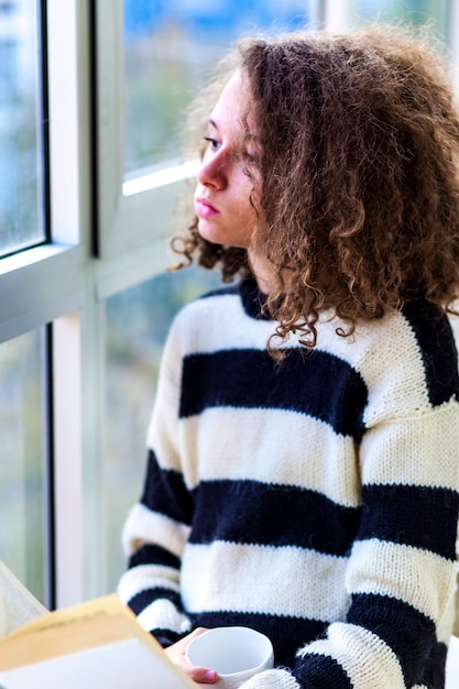 Nastoletnia dziewczyna z kubkiem przez okno