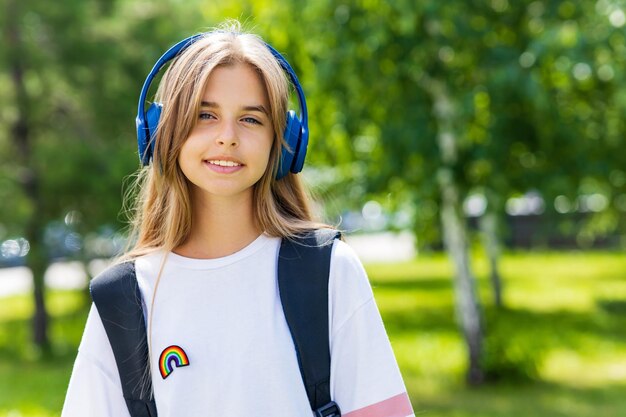 Nastoletnia dziewczyna z plecakiem i zestawem słuchawkowym w parku z powrotem do koncepcji szkoły
