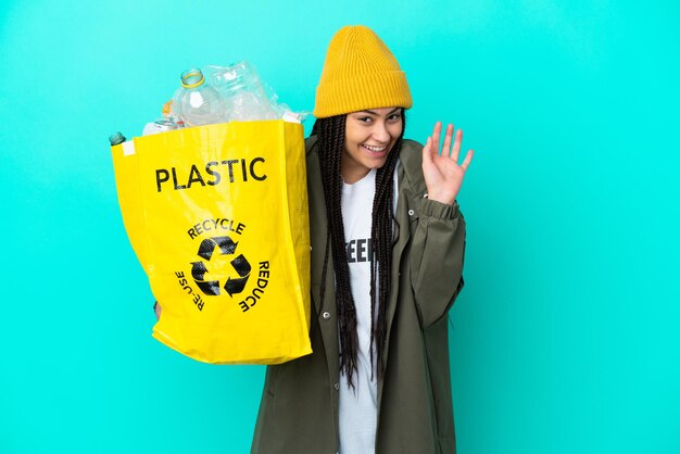 Nastoletnia dziewczyna z warkoczami trzyma torbę do recyklingu, salutując ręką ze szczęśliwym wyrazem twarzy