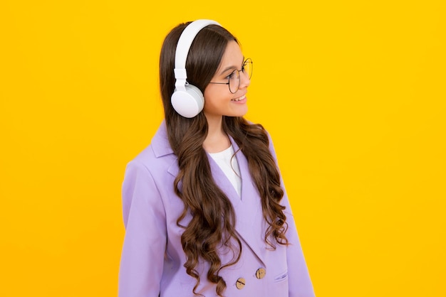 Nastoletnia dziewczynka w słuchawkach słuchająca muzyki w stylowym, swobodnym stroju izolowanym na żółtym tle