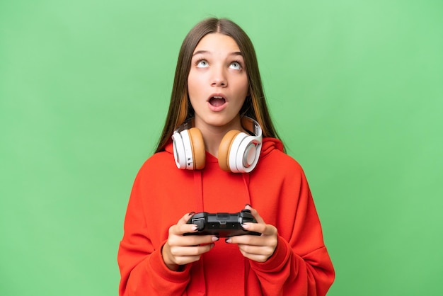 Nastoletnia kaukaska dziewczyna bawi się kontrolerem gier wideo na odizolowanym tle, patrząc w górę i ze zdziwionym wyrazem twarzy