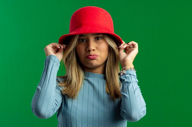 Zdjęcie nastoletnia kobieta w studiu fotograficznym z zielonym tłem robi pozy i wyrazy twarzy i nosi czerwony kapelusz