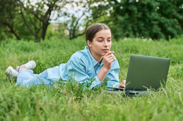 Nastoletnia studentka leżąca na zielonej trawie za pomocą laptopa Koncepcja dorastania w technologii edukacji w szkole średniej