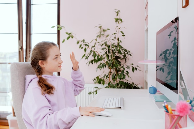 Nastoletnia uczennica rozmawia na czacie wideo na komputerze stacjonarnym, siedząc przy biurku w swoim pokoju