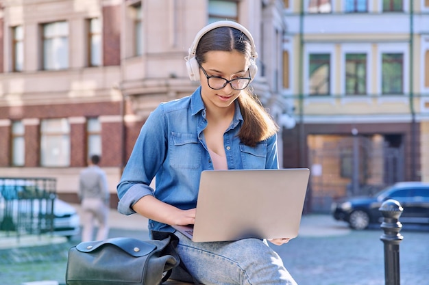 Nastoletnia Uczennica W Słuchawkach Za Pomocą Laptopa Na Zewnątrz Tła Miejskiego