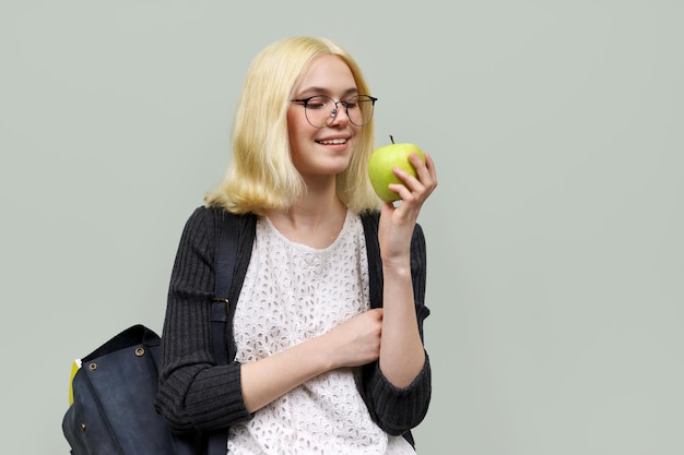 Nastoletnia uczennica z plecakiem z zielonym jabłkiem w dłoni na jasnym tle Nastolatki szkoła kolegium zdrowa żywność edukacja i wiedza