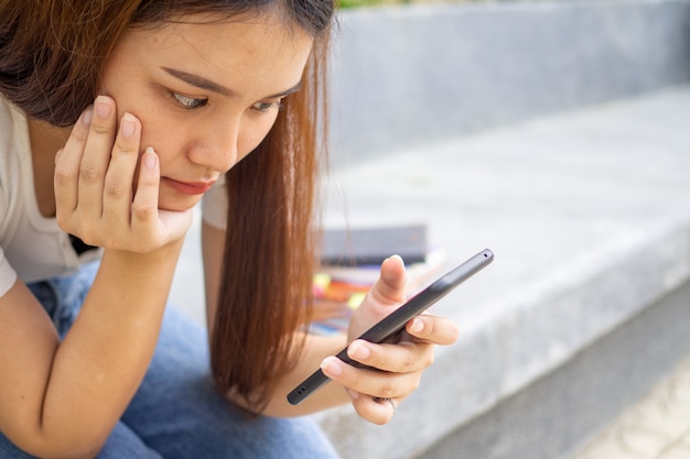 Nastoletnie dziewczyny siedzą i patrzą na telefon trzymany w rękach, niestety czekając na telefon lub wiadomość od swojego chłopaka.