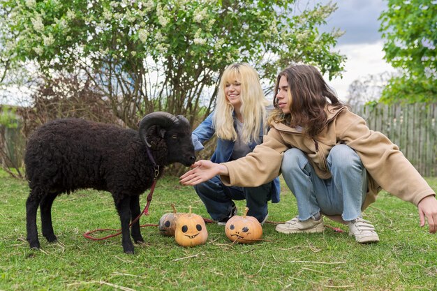 Nastoletnie nastolatki i czarny domowy baran z halloweenowymi dyniami na trawie