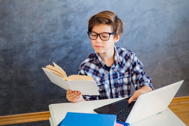 Nastoletniej chłopiec czytelnicza książka i use laptop w domu