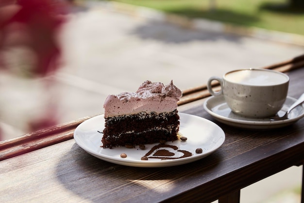 Nastrojowy naturalny kawałek ciasta i szklanka cappuccino na drewnianym stole na tarasie kawiarni Estetyczny czas na kawę Czas dla siebie Twarde cienie