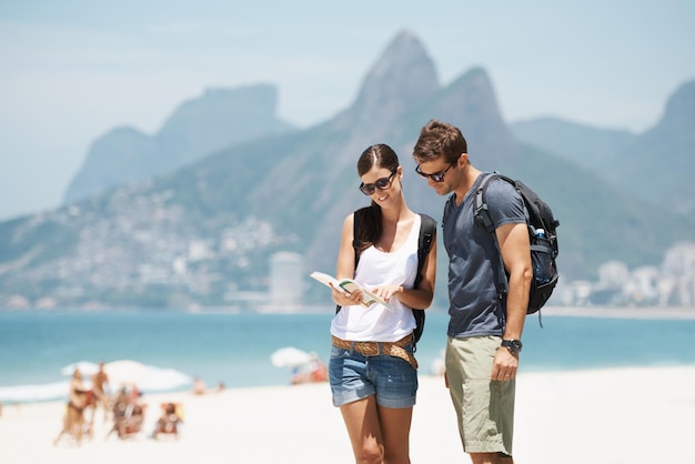 Nasze położenie w raju Ujęcie młodej pary patrzącej na mapę, stojąc na plaży