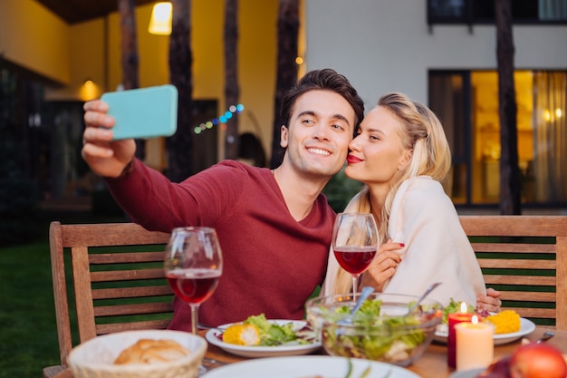 Nasze zdjęcie. Radosny miły mężczyzna uśmiecha się podczas robienia selfie ze swoją dziewczyną w restauracji