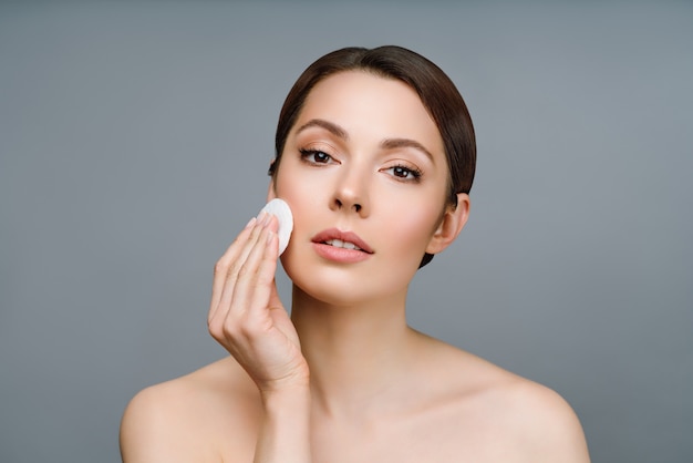 Naturalna kobieta o dobrej skórze oczyszcza twarz kosmetycznym wacikiem kosmetycznym