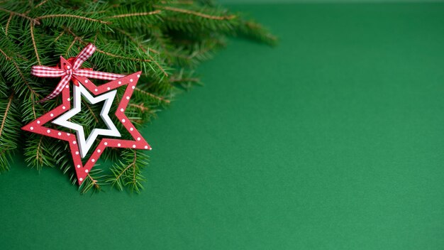 Naturalny bukiet gałązek jodły i zabawka drewniana czerwono-biała gwiazda leżą na zielonym tle.