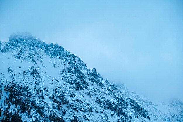 Naturalny krajobraz śnieżnej góry z skałami i drzewami w pochmurny dzień przedstawiający zjawisko geologiczne z zamarzającą czapką lodową i chmurami kumulusowymi na elektrycznie niebieskim niebie Morskie Oko Polska