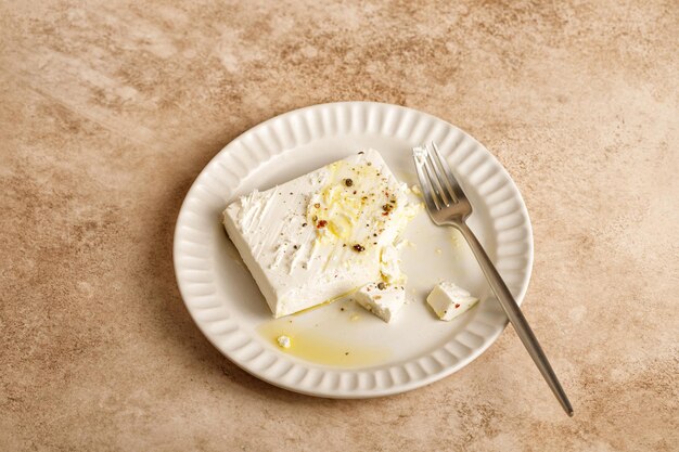 Naturalny marynowany grecki ser feta na białym talerzu z oliwą i pieprzem ziołowym Widelec beżowy stół