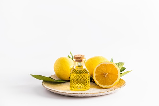 Naturalny organiczny olejek cytrynowy w wypukłej szklanej butelce z korkiem stoi na talerzu ze świeżymi owocami z przodu na tekst
