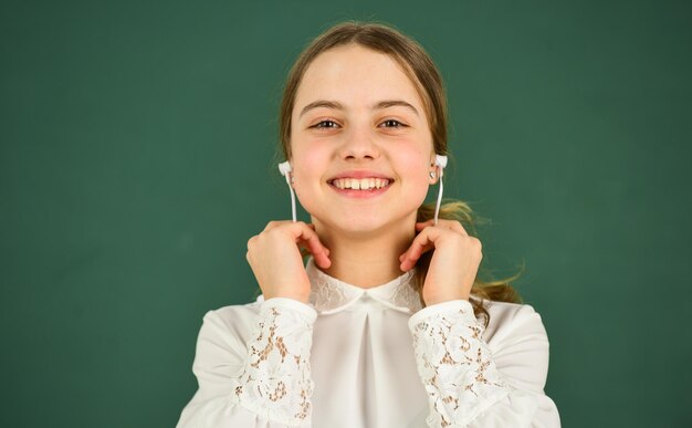 Nauczanie domowe edukacja online Dziewczyna w słuchawkach słucha muzyki Słuchanie książki audio Uczennica w słuchawkach na tablicy tło kopia przestrzeń Tłumaczenie audio Koncepcja uczenia się audio