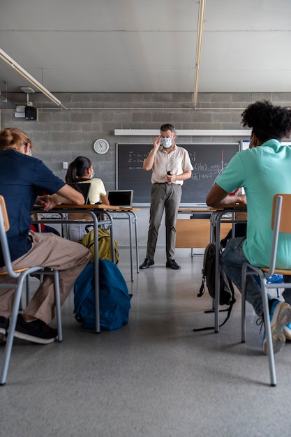 Nauczyciel noszący maskę na twarz Wielorasowi nastolatki licealiści słuchają lekcji Edukacja