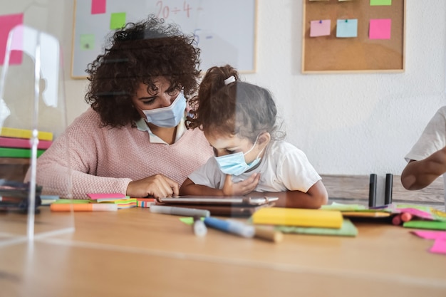 Nauczyciel używający tabletu z dziećmi w wieku przedszkolnym podczas epidemii koronawirusa – skoncentruj się na kobiecej dłoni