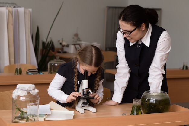 Nauczycielka i uczennica mała dziewczynka siedzi w szkolnej klasie biologii i pracuje z mikroskopem